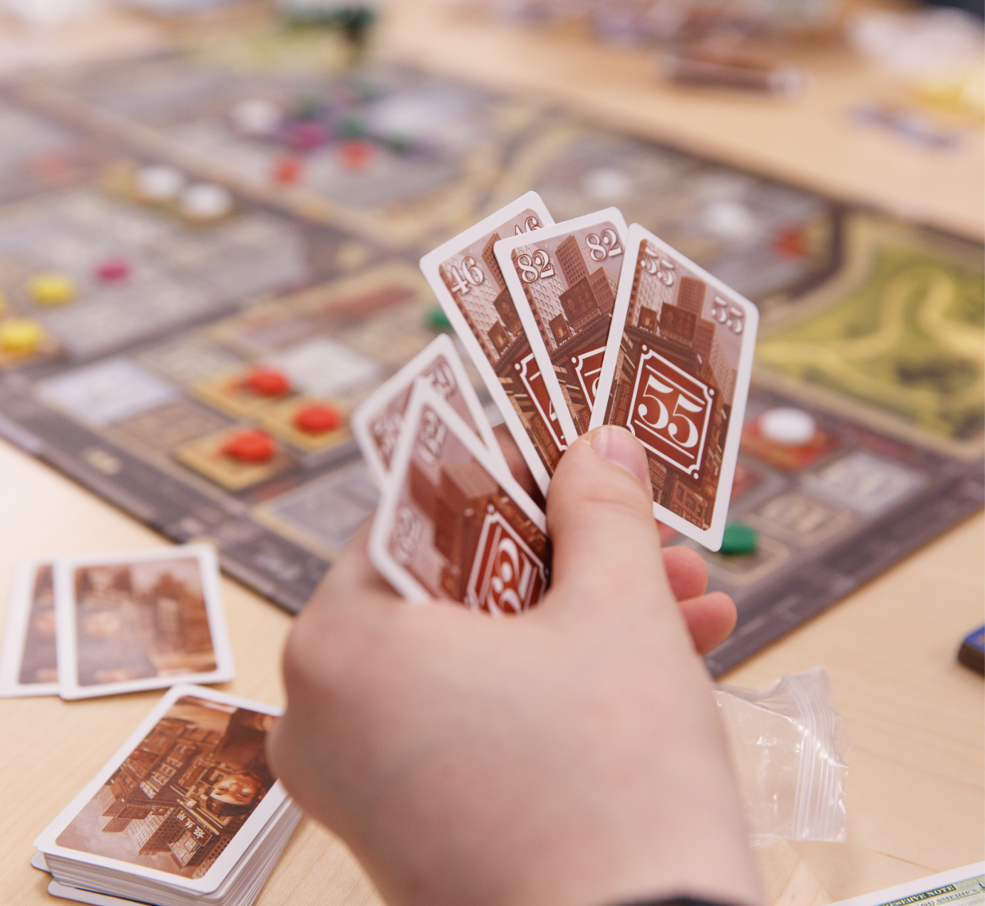 A hand holding cards over a table with a board game