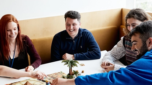 Five people playing a board game together and laughing