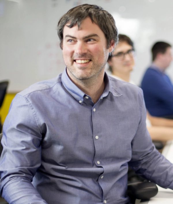 A man smiling while in a room of people in the office