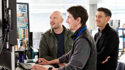 Three people looking at trading desk monitors