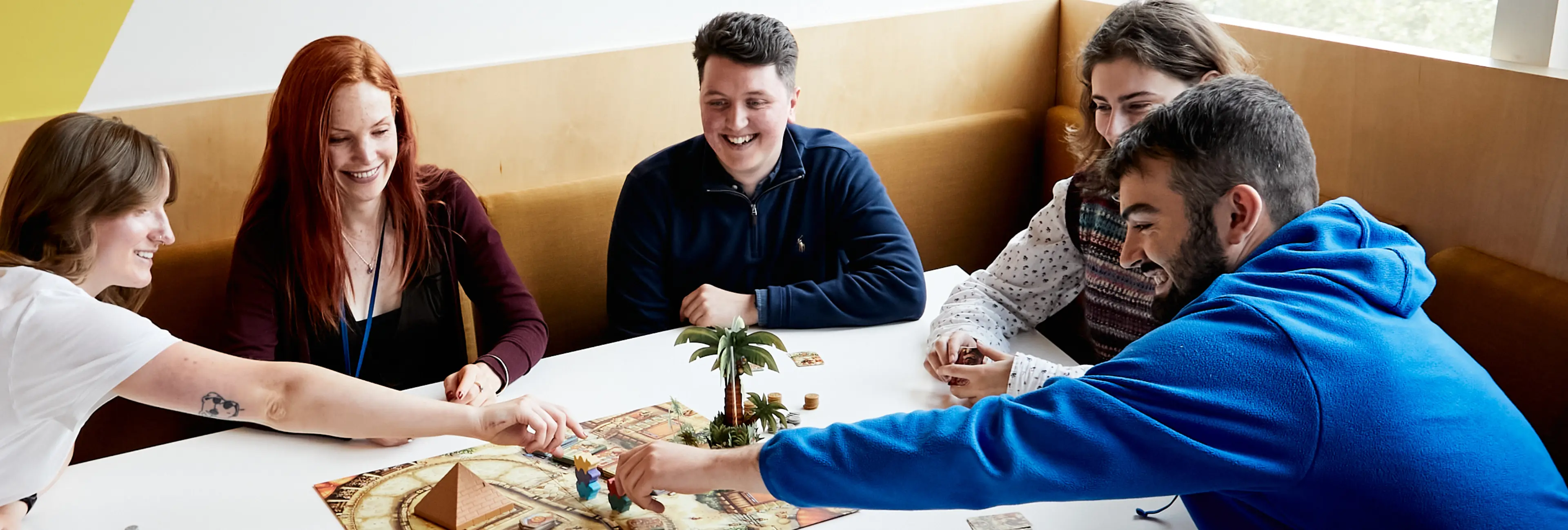 Five people playing a board game together and laughing